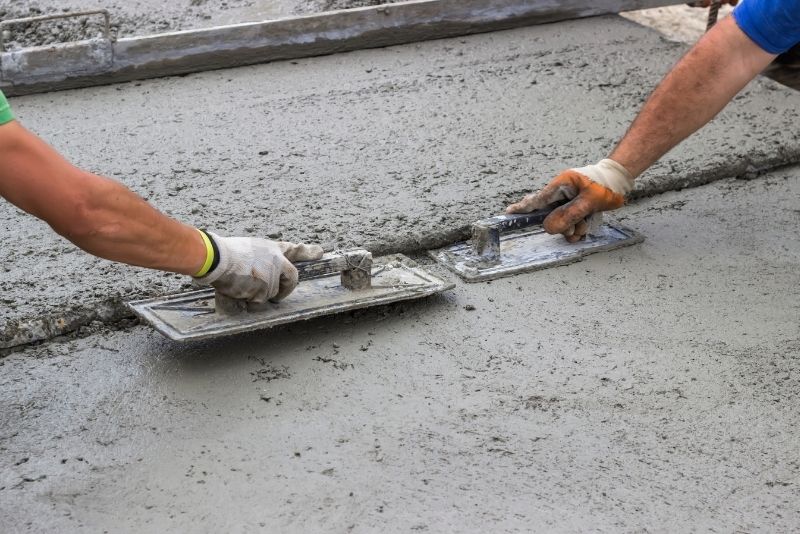 2 concrete specialist holding both hands a trowel on top of a concrete ground